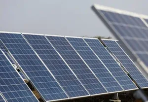 A row of angled solar panels mounted on a metal racking system in an open outdoor field, with one panel blurred in the foreground for depth.